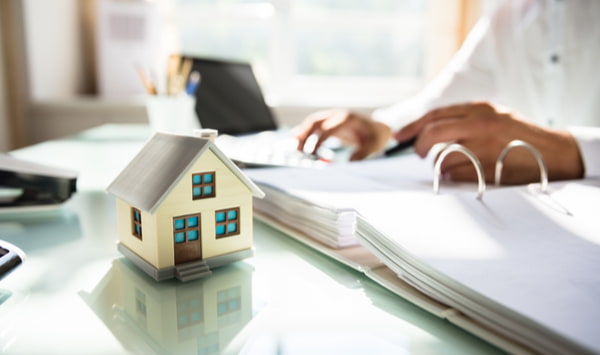 Businessman's hand calculating invoice with house model in office